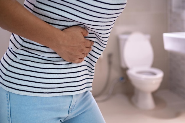 Frauen stehen vor der Badezimmertür und halten mit ihren Händen den Bauch mit starken Bauchschmerzen oder Durchfall Das Konzept der Magenkrämpfe Durchfall
