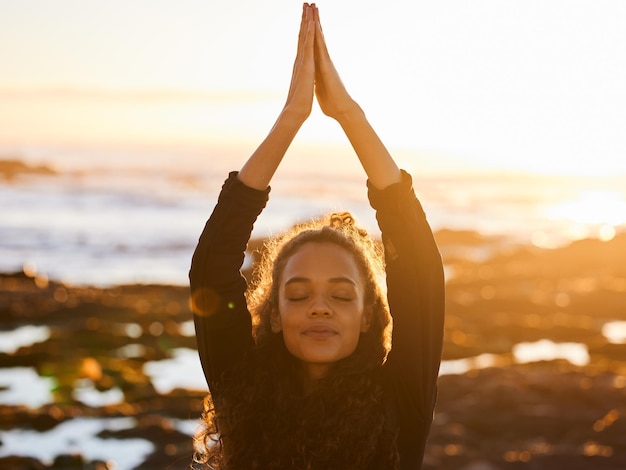 Foto frauen-strand-yoga und sonnenuntergang mit betenden händen, geschlossenen augen und seelenfrieden im sommersonnenschein. mädchen-zen-meditation und achtsamkeit für gesundheit, wellness und bewegung am meer mit stretching im freien