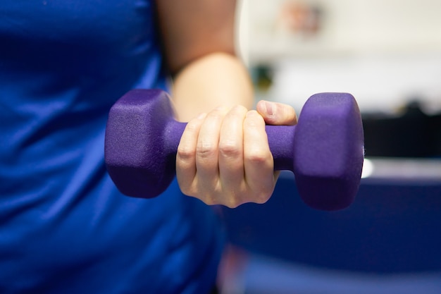 Frauen tragen Sportuhr halten Hantel mit einer Hand Kraftlippe für Brust Bizeps Muskel Gewicht Training Indoor Unschärfe Hintergrund