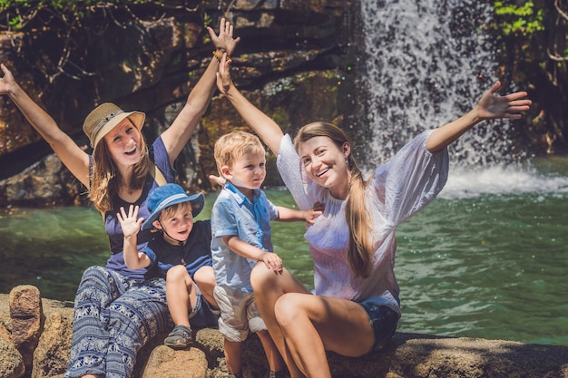 Frauen und Kinder in der Nähe eines Wasserfalls mit erhobenen Händen