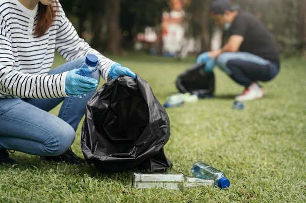 Frauen und Männer lagern im Morgenlicht Plastikmüllflaschen in schwarzen Säcken im Park