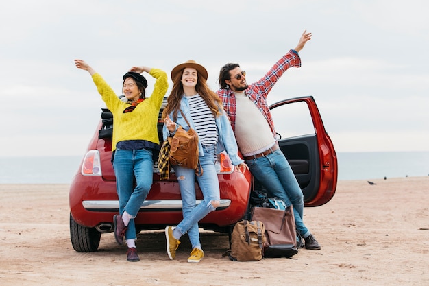 Frauen und Mann mit erhobenen Händen in der Nähe von Auto am Strand