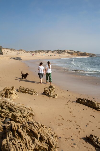 Frauen zu Fuß am Felsen am Strand von Carreiro da Fazenda, Vila Nova de Milfontes, Portugal