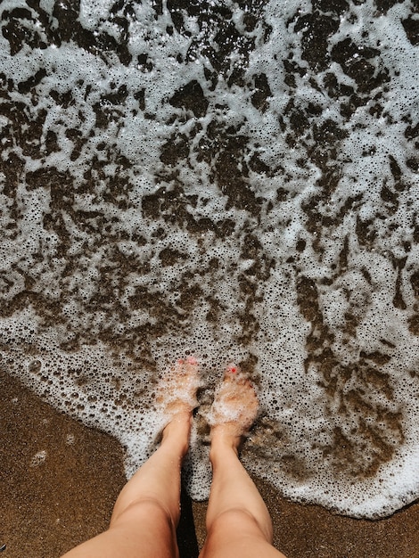 Frauenbeine barfuß am Meer Schaumwellen am Sandstrand Sommertag. Draufsicht über Frauenfüße women