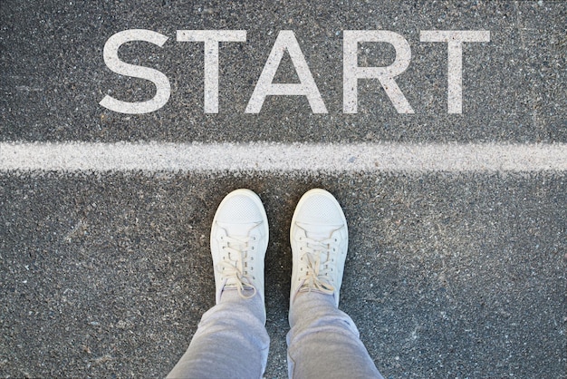 Foto frauenbeine in weißen turnschuhen stehen auf dem asphalt und tragen das wort „start“ darauf. ein angehender geschäftsmann. lasst uns beginnen. es ist ein neuanfang. füße an der startlinie