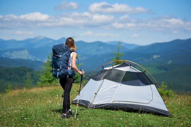 Frauencamper nahe Zelt auf der Spitze eines Hügels gegen blauen Himmel und Wolken, wegschauen, sich nach dem Wandern ausruhen, Sommertag in den Bergen genießen