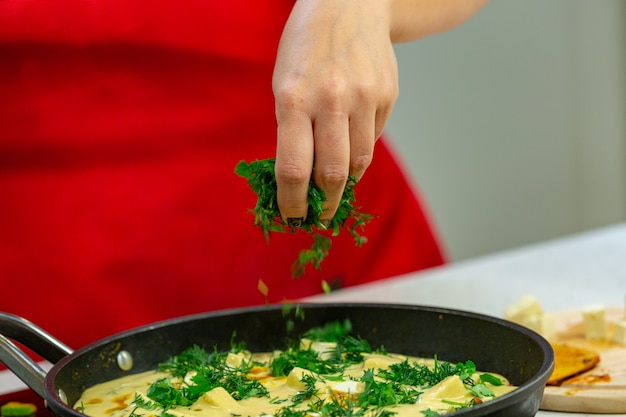 Frauenchef, der Omelett mit Kräutern an einer Küche zubereitet. Hände hautnah