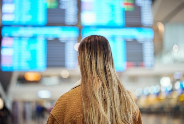 Frauenflughafen und Lesetafelbildschirm und Flugplan für Reiseflugzeug und Abenteuer mit Rücken Mädcheneinwanderung und globaler Transport in der Lobby für Abflug oder Ankunft der Flugzeugzeit