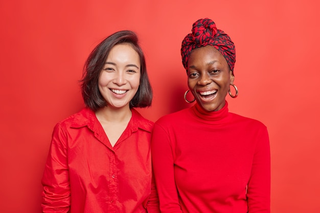 Frauenfreunde lächeln positiv genießen schönen Tag verbringen Freizeit zusammen tragen leuchtend rote Kleider stehen nebeneinander auf lebendigem Studio