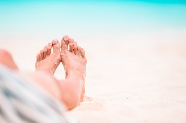 Frauenfüße auf dem weißen Sandstrand im seichten Wasser