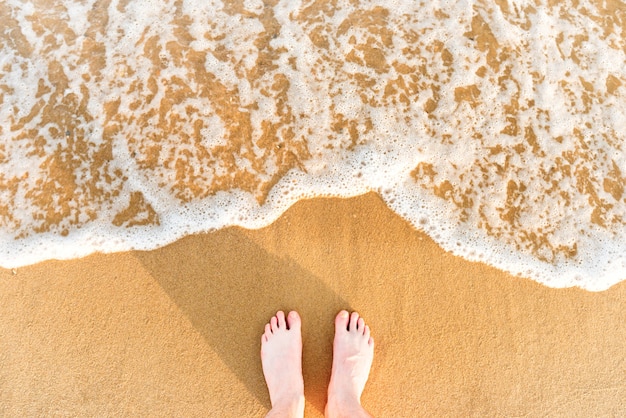 Frauenfüße auf gelbem Strandsand mit Meereswelle und weißem Schaum