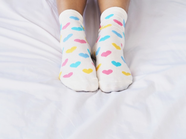 Frauenfüße, die weiße Socke mit Pastellherzformmuster tragen