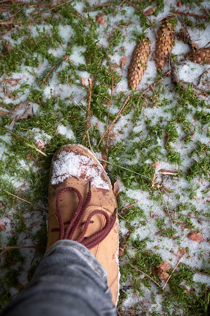 Frauenfuß in den Reisestiefeln auf einem moosigen schneebedeckten Boden im Winterwald. Reisekonzept.