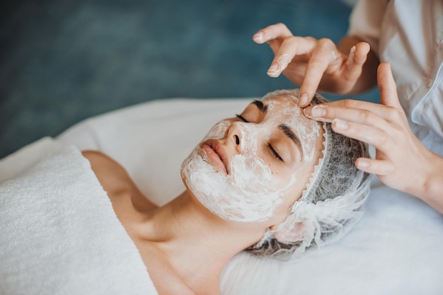 Foto frauengesicht, das gesichtspflege mit creme durch kosmetikerhände im spa-salon-nahaufnahmeporträt erhält