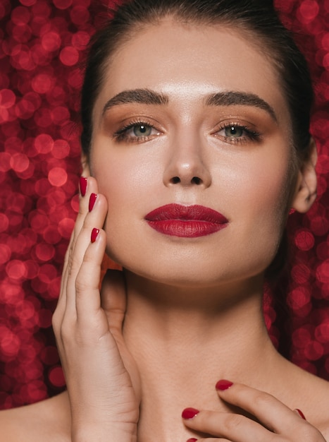 Frauengesichtsparteischönheit roter Lippenstift saubere Haut schöner weiblicher Zauber. Hintergrund mit roten Pailletten