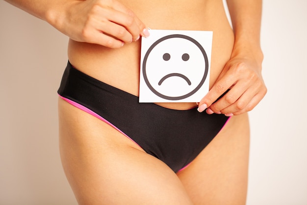 Frauengesundheit, weiblicher Körper, der traurige Lächeln-Karte nahe Magen hält.