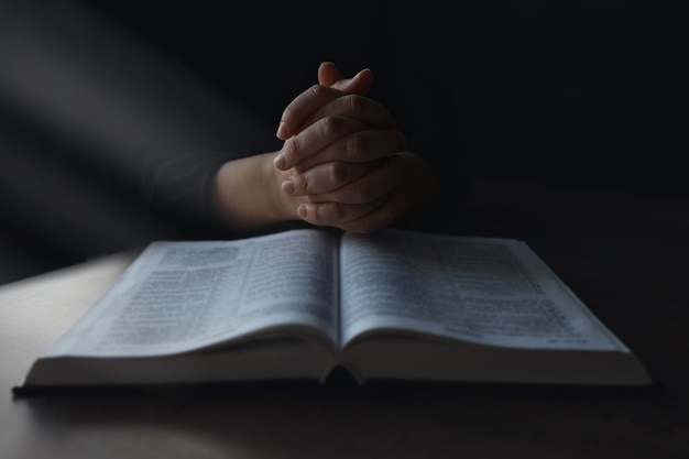 Frauenhände auf Bibel. Sie liest und betet über die Bibel in einem dunklen Raum über einem Holztisch.