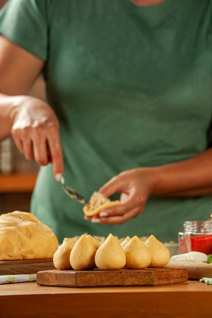 Frauenhände, die brasilianische krokette coxinha de frango auf einem holztisch vorbereiten