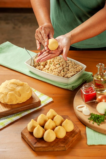 Frauenhände, die brasilianische krokette coxinha de frango auf einem holztisch vorbereiten