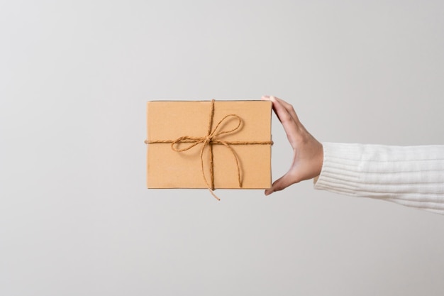 Frauenhände, die eine Geschenkbox mit einer Schleife halten Konzept des minimalistischen Stils der Geschenkbox