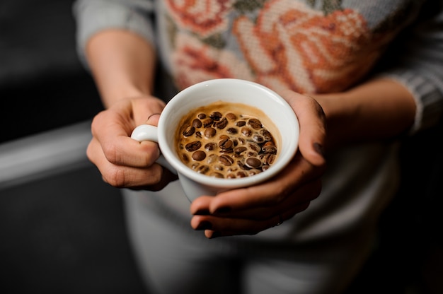 Frauenhände, die eine weiße Schale frischen und aromatischen Kaffee halten