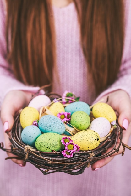 Frauenhände, die gemaltes Osterei in einem kleinen Nest halten, tonten selektiven Fokus des Bildes