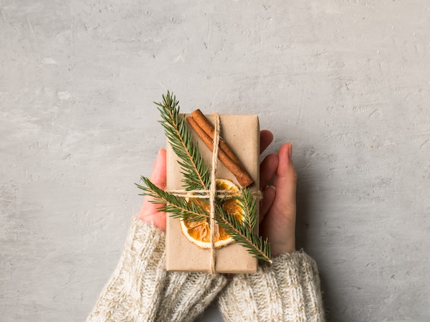 Frauenhände, die Weihnachtsgeschenkbox im grauen Beton halten