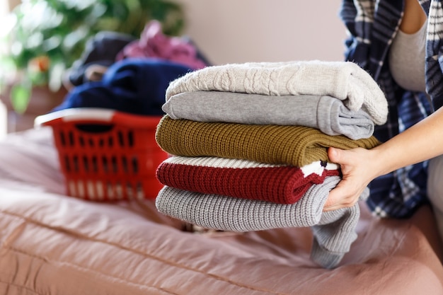 Frauenhände falten Kleidung, stricken gemütliche Pullover in einem Schlafzimmer, sammeln nach der Wäsche.Haushälterin-Konzept