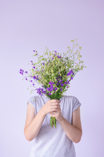 Frauenhände halten einen großen Strauß Wild- und Wiesenblumen vor einem Hintergrund schlichter Wände