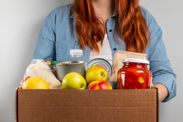 Frauenhände halten Lebensmittelspendenbox mit Früchten, Müsli, Wasser und verschiedenen Konserven