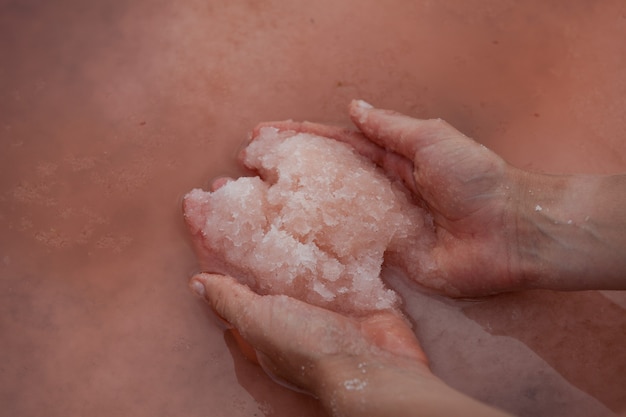 Frauenhände halten rosa Salz an der Wasseroberfläche eines einzigartigen rosa Sees. Die ursprüngliche Farbe des Sees wird durch die halophile Mikroalge Dunaliella salina gegeben. Rosa Salz wird in der Kosmetik und Volksmedizin verwendet.