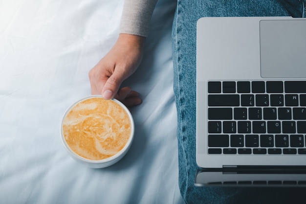 Foto frauenhände halten tasse kaffee latte zu hause und überprüfen ihren laptop