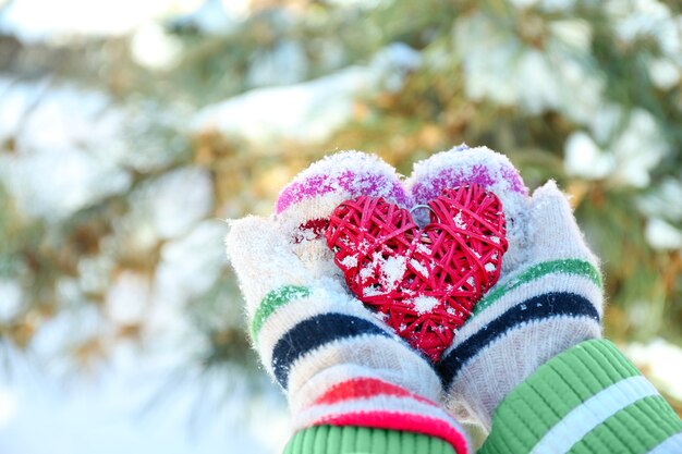 Frauenhände in gestrickten Handschuhen, die rotes Herz auf Winter halten