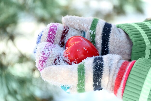 Frauenhände in gestrickten Handschuhen, die rotes Herz auf Winterhintergrund halten