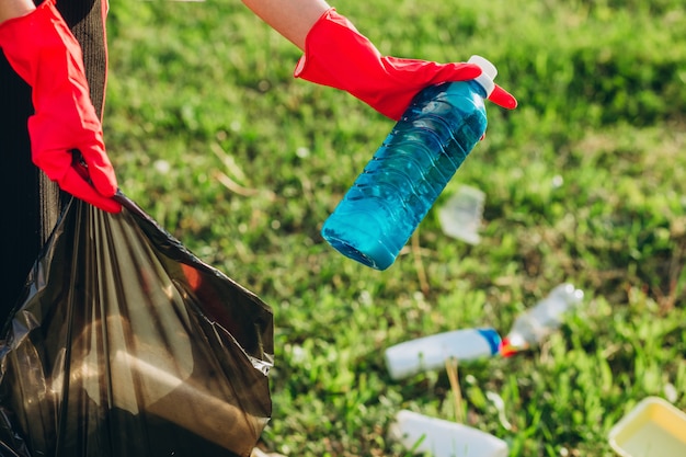 Frauenhände in roten Gummihandschuhen. Frau sammelt Müll in der Tasche. Freiwilliger Müll im Sommerpark. Nette progressive Frau, die sich bemüht, der Umwelt zu helfen