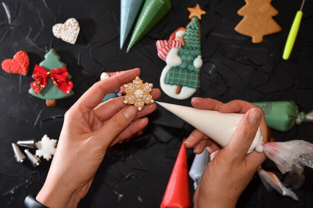 Frauenhände malen Ornamente auf Weihnachtsleckereien Weihnachtsvorbereitungen Hände schmücken handgefertigte Weihnachtslebkuchen mit Glasur Puderzucker Weibliche Hände malen Weihnachtslebkuchen Draufsicht