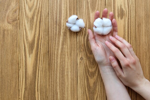 Frauenhände mit Baumwollblumen auf einem Holztisch