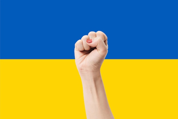 Frauenhände mit Faustgeste auf farbigem Hintergrund der ukrainischen Flagge