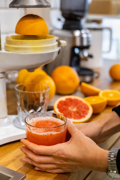 Frauenhände mit ganzen und halben frischen reifen orangen und grapefruits, die detox-saft auf dem tisch kochen