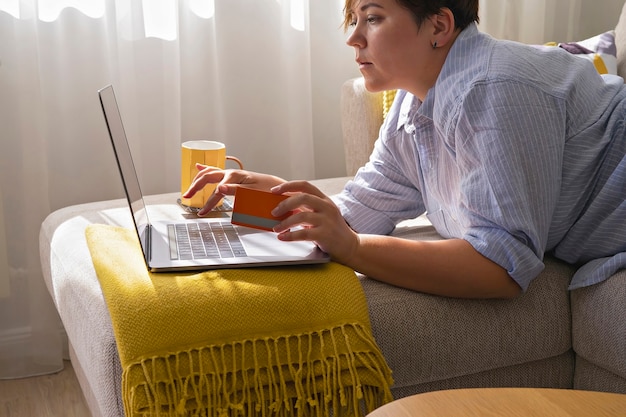 Frauenhände mit Kreditkarte und Laptop beim Online-Shopping. Gemütliches Interieur in hellen Farben während des Herbstverkaufs. Black Friday und Cyber Monday Konzept