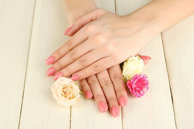 Frauenhände mit rosa Maniküre und Blumen auf Holzhintergrund