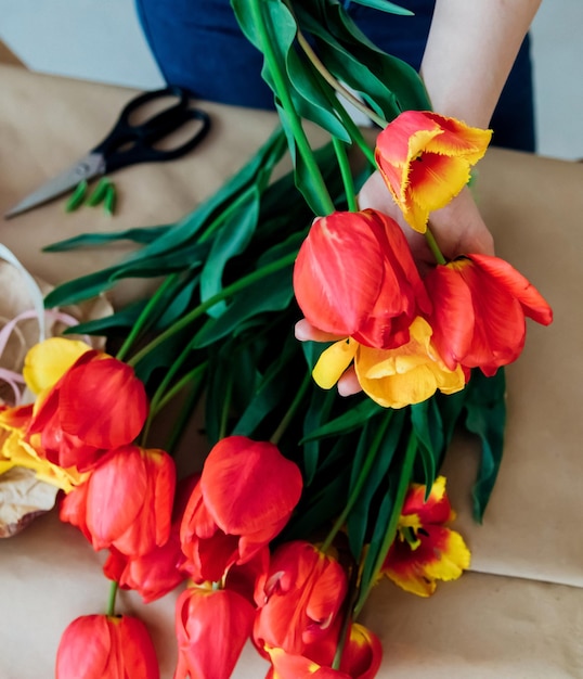 Frauenhände packen einen festlichen Blumenstrauß in Geschenkpapier Der Florist macht eine Montage mit roten Tulpen in der Werkstatt Eine Frau bei der Arbeit Kleinunternehmen oder Hobby