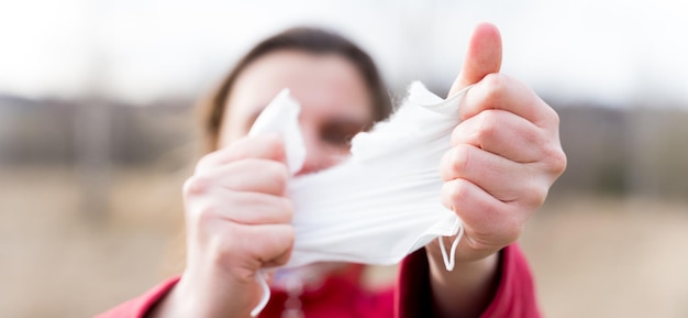 Frauenhände reißen schützende medizinische Einweg-Gesichtsmaske auseinander Ende der Quarantäne und Selbstisolierung aufgrund einer covid19coronovirus-Pandemie Ausgang von zu Hause auf die Straße Gehen Sie an der frischen Luft in der Natur