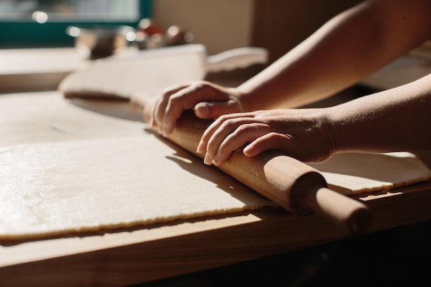Frauenhände rollen Teig in Mehl mit Nudelholz in der Bäckerei aus