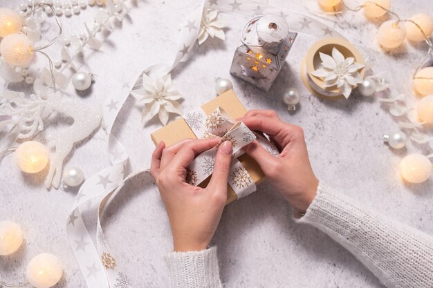 Frauenhände schmücken Weihnachtsgeschenk mit weißem Band und dekorieren Weihnachten und Neujahr
