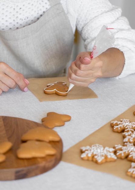 Frauenhände schmücken Zuckerguss hausgemachte traditionelle Neujahrskekse Schneeflocke Lebkuchenmann