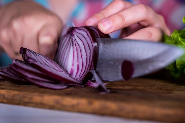 Frauenhände schneiden eine rote Zwiebel mit einem großen Messer auf einem Schneidebrett