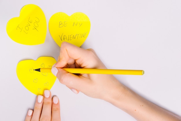 Frauenhände schreiben Liebesbrief auf leuchtende Notenherzen für St.Valentines Day.