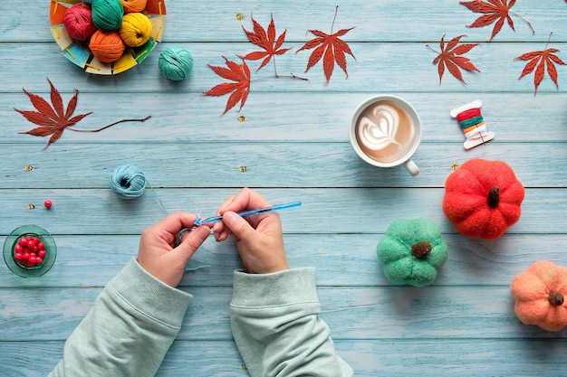 Frauenhände stricken häkeln. Draufsicht mit Garnkugeln, Wollbündeln, dekorativen Herbstkürbissen und Herbstlaub.