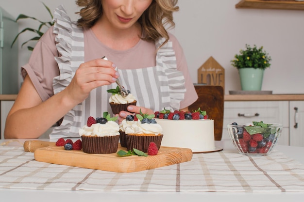 Frauenhände verzieren Cupcakes mit Sahne. Konditorberufskonzept.